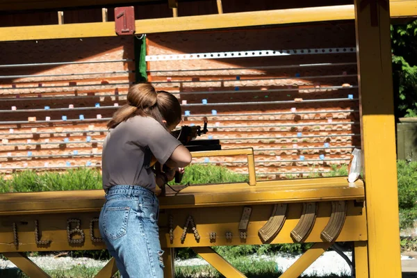 A woman with a gun is aiming through the scope at a target in a shooting range.