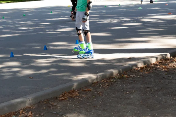 A boy on roller skates with elbow pads and knee pads is standing on the training ground.