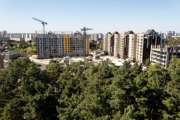 Şehir manzarası. Yeşil ağaçlar arasında çok katlı çok katlı binalar inşa ediliyor. Turnalar evlerin yanında görünüyor..