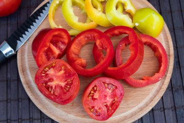 Yuvarlak tahtada iki çeşit doğranmış biber ve domates dilimi vardır. Yakında bir bıçak var.