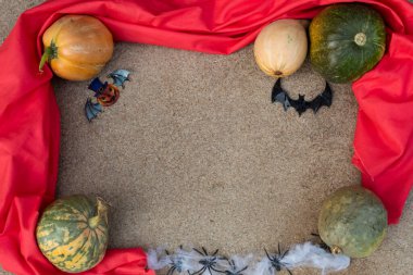 Kırmızı bir kumaş çerçevesinde, balkabakları, ağdaki örümcekler, bir yarasa ve kağıttan kesilmiş bir balkabağı vardır..