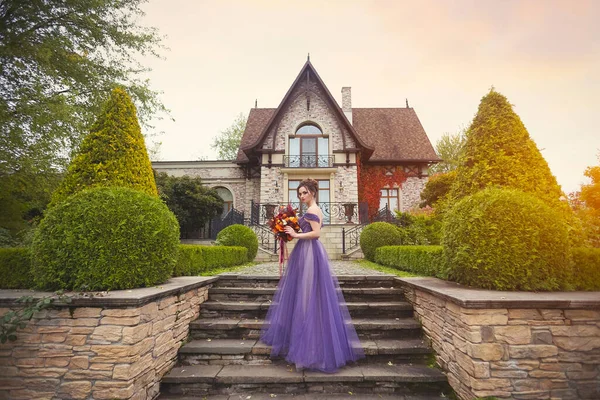 A girl in a lilac dress standing on the background of an art Nouveau cottage in the autumn garden