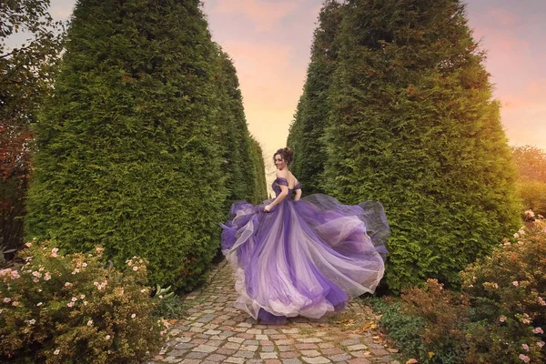 A beautiful young girl in a lilac dress running down the alley of the autumn park. Romantic evening photo.