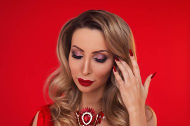 Parlak makyajlı, kırmızı dudaklı güzel bir sarışın kız portresi ve kırmızı arka planda sahte elmaslar olan bir kolye.