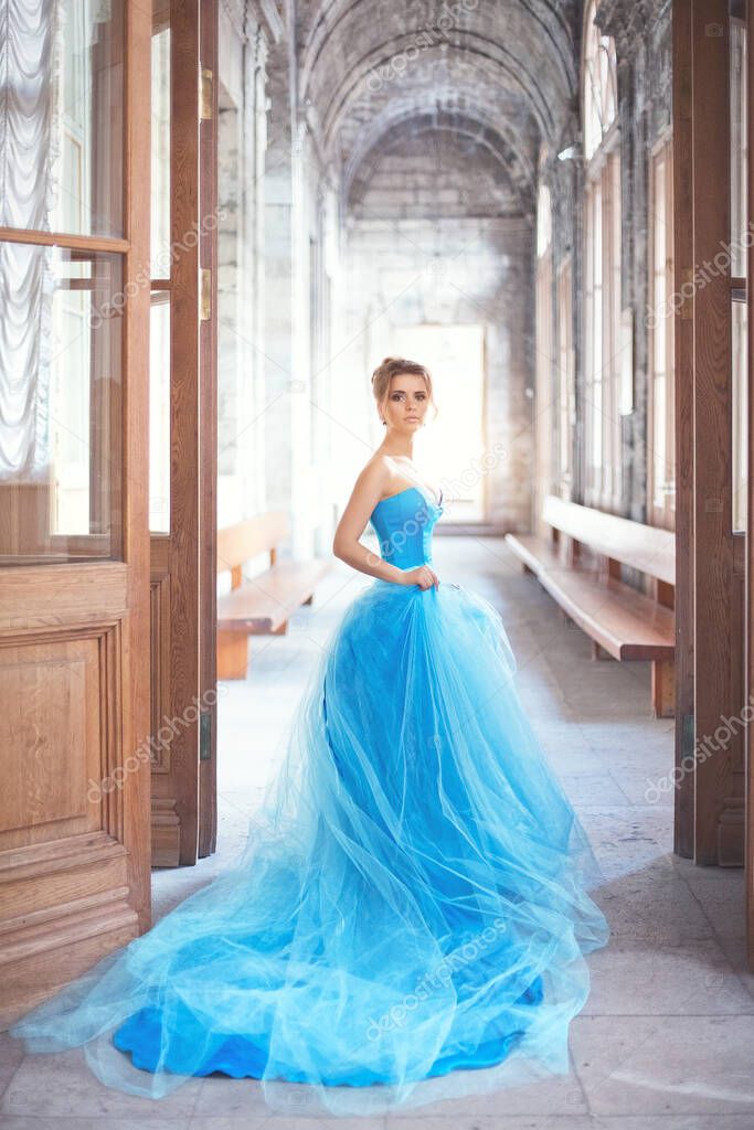 A beautiful young girl in a blue ball gown standing in the doorway of an ancient manor