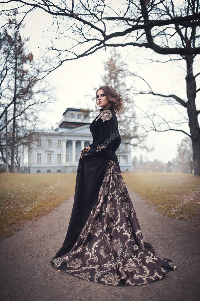 Beautiful young girl in a long vintage dress standing against the background of an old manor. Romantic autumn portrait.