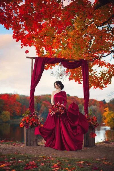 Piękna Panna Młoda Ciemnoczerwonej Sukience Stoi Pod Dużym Pojedynczym Drzewem — Zdjęcie stockowe