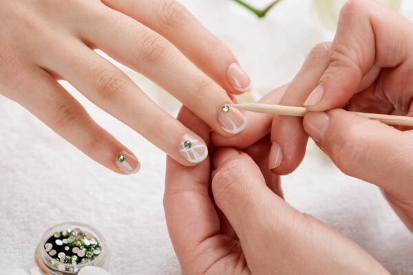 Beautician attaching green rhinestones on nails. Chic and fabulous design over French manicure base.