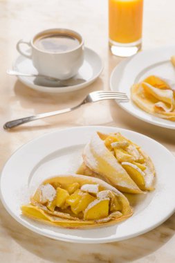 Elma dolgu ile Pancakes ile pudra şekeri serpilir. Bir fincan kahve bir fincan tabağı, bir çorba kaşığı, bir bardak meyve suyu arka planda. Otel kahvaltı.
