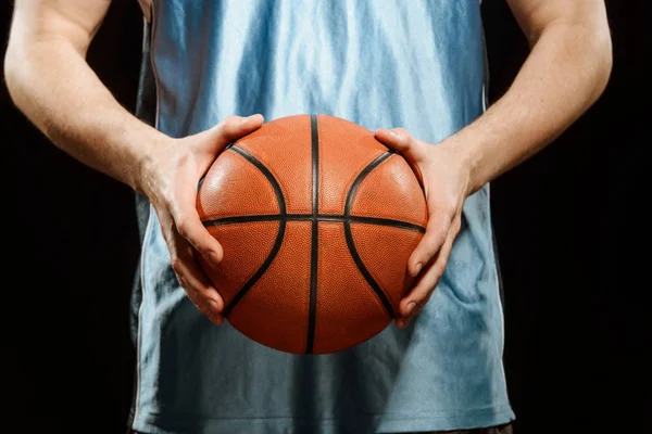 Basketball in hands of player. Close-up shot on a ball being held by a sportsman, isolated on black.