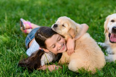 Kız onun köpekleri bahçeye oynamaya. Şirin çocuk gülümser ve bir golden retriever köpek yavrusu sarılma.