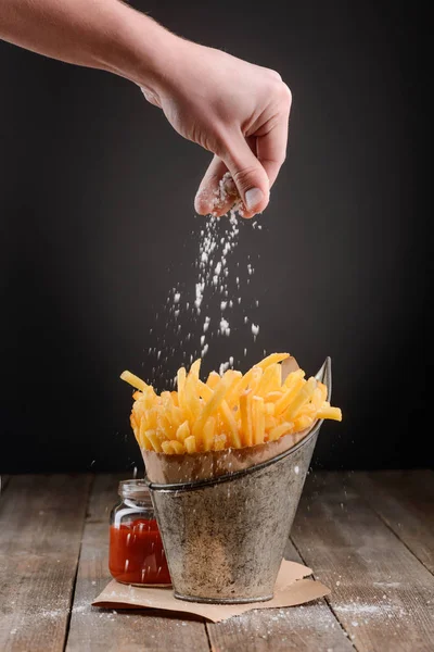 Mão polvilha sal em batatas fritas — Fotografia de Stock