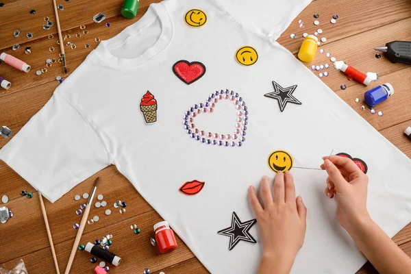 Girl sewing patches on t-shirt. — Stock Photo, Image