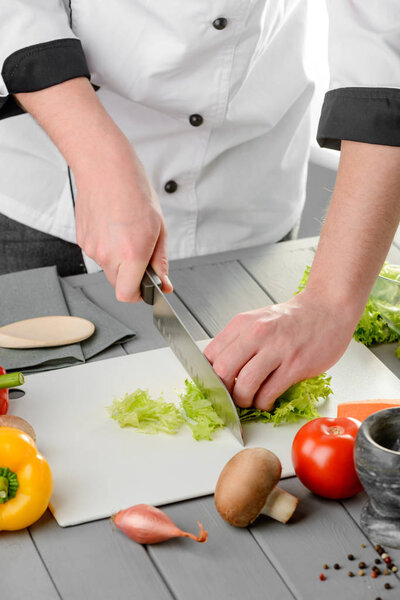 Chef chopping lettuce leaves and cutting vegetables for a salad. Cooking process in a restaurant.