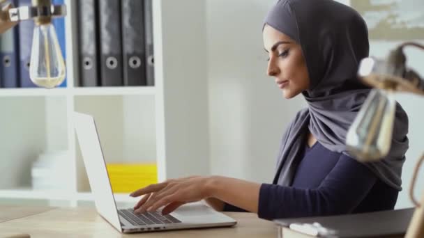 Muslimische Geschäftsfrau arbeitet an einem Laptop, tippt auf einer Tastatur und schreibt einen Text. Stilvolles formales Outfit mit Hijab. — Stockvideo