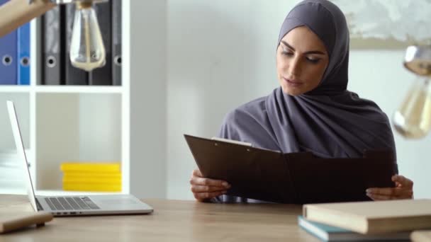 Muslim lady working in the office. Woman reading documents, then showing her gorgeous smile. — Stock Video