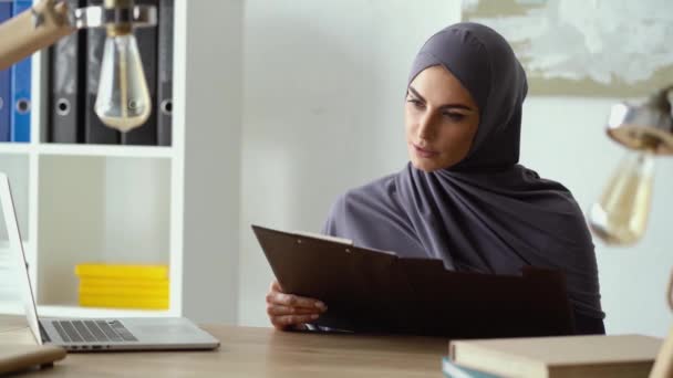 행복 한 이슬람 사업가가 그녀의 사무실에서 일하고 있습니다. 문서를 보고 있다가 미소를 짓는 사람들. — 비디오