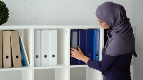 Λογιστής που ψάχνει για ένα φάκελο με πραγματικές πληροφορίες στο ράφι. Νεαρή Μουσουλμάνα που εργάζεται στο γραφείο. — Αρχείο Βίντεο