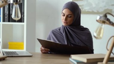 Müslüman kadın belgelerle çalışıyor ve düşünceli bir bakış atıyor.