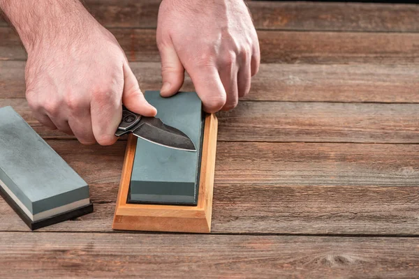 Man sharpening his pocket knife with a whetstone on a rustic wooden table