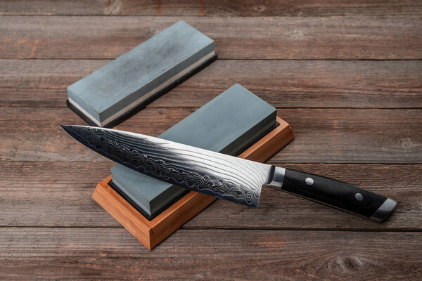 Chefs knife and whestones on rustic wooden background