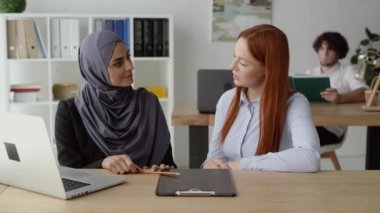 İki bayan iş arkadaşı ofiste bir şey tartışıyor.