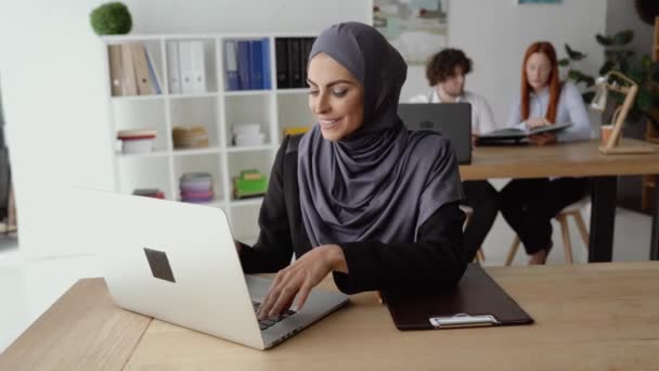 Muzułmanka pracująca na laptopie w biurze ze swoimi chrześcijańskimi współpracownikami — Wideo stockowe