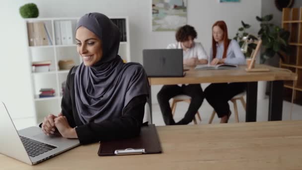 Glimlachende moslim vrouw typen op een laptop toetsenbord in het kantoor — Stockvideo