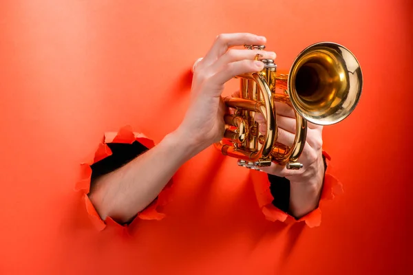 Mãos tocando trompete rasgado buracos no fundo papel vermelho — Fotografia de Stock