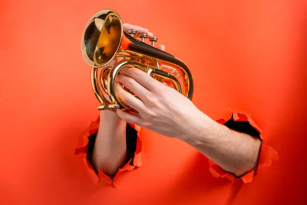 Mãos tocando trompete de bolso rasgado buracos no fundo papel vermelho — Fotografia de Stock