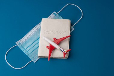 Mavi arka planda uçak oyuncağı, pasaport ve sağlık maskesi.