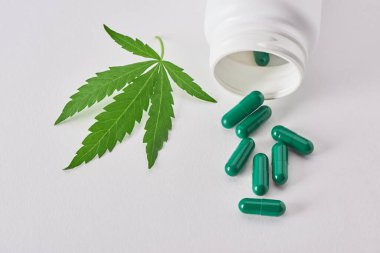 Beyaz arka planda kenevir yaprağı ve bir şişe yeşil kapsül.