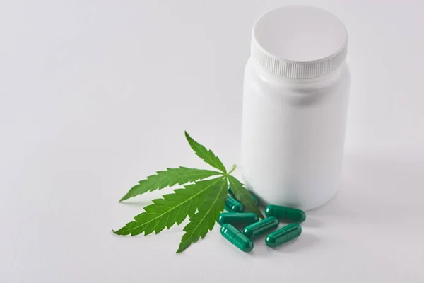 Un frasco de pastillas, cápsulas y hojas de marihuana sobre fondo blanco — Foto de Stock
