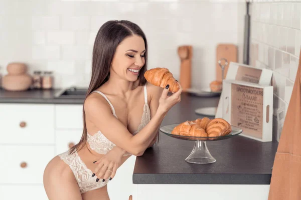 Mujer joven seductora en ropa interior de encaje blanco comiendo un croissant fresco —  Fotos de Stock