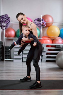 Genç bir kadın çocuğuyla spor salonunda oynuyor.