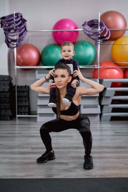 Anne çocuğuyla spor salonunda çömeliyor.