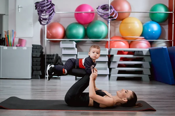 Beautiful fit woman and her kid doing exercises together in the gym