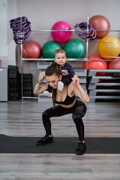 Genç anne, küçük oğluyla birlikte arkada çömeliyor.