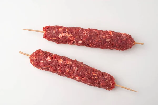 Minced beef meat on wooden skewers on white background — Stock Photo, Image