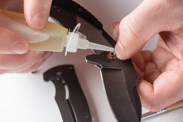 Close-up em reparadores mãos lubrificando uma faca de bolso com óleo doméstico — Fotografia de Stock