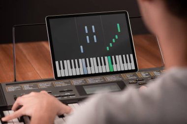 Çocuk piyano çalmayı öğreniyor ve tabletinde bir uygulama kullanıyor.