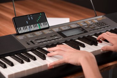 Çocuk piyano çalıyor ve öğrenmek için telefonunda bir uygulama kullanıyor.