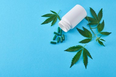 Kenevir yapraklarının arasına dökülmüş kapsülleri olan beyaz bir şişenin üst görüntüsü.