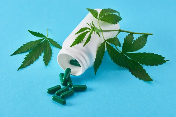 Hojas de marihuana, una botella blanca y cápsulas verdes sobre fondo azul — Foto de Stock