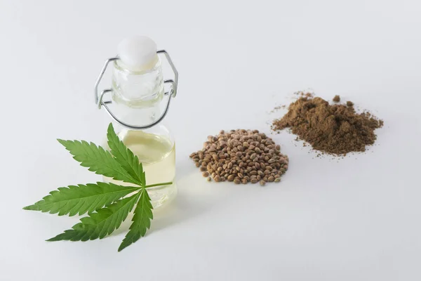 Una hoja de cáñamo, una botella de aceite de semillas de cáñamo, semillas y un puñado de harina en blanco — Foto de Stock