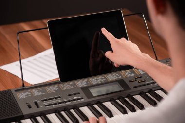 Genç adam piyano çalıyor ve tabletinde öğrenme uygulaması kullanıyor.