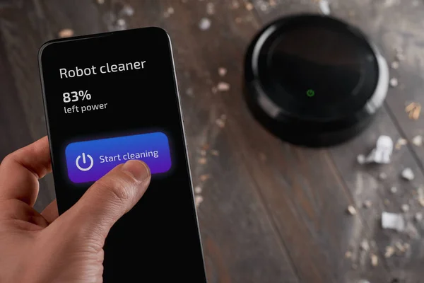 Man tapping a button on his phone and turning on a robot cleaner