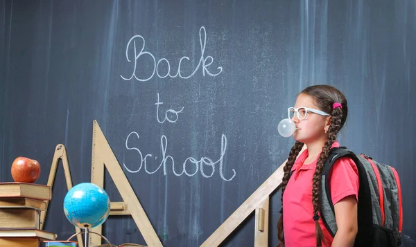 Happy school girl in front of the blackboard