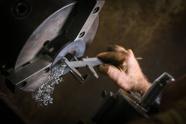 Worker professionally measuring the shaped material on lathe