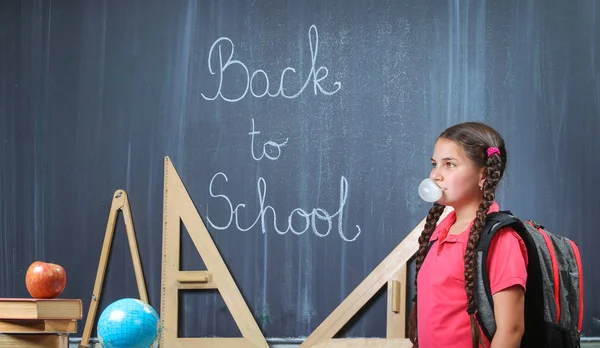 Happy school girl in front of the blackboard